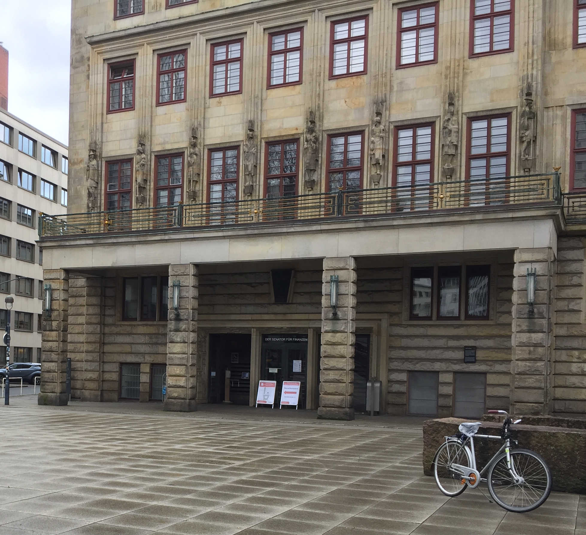 <p>Ein silbernes Fahrrad steht vor dem nass geregneten Platz vorm Eingang des "Haus des Reichs" in Bremen</p>